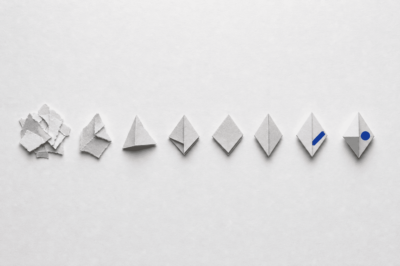Eight small paper forms in a row progressing from a loose pile of scraps on the left to one crisply folded resolved form on the right.