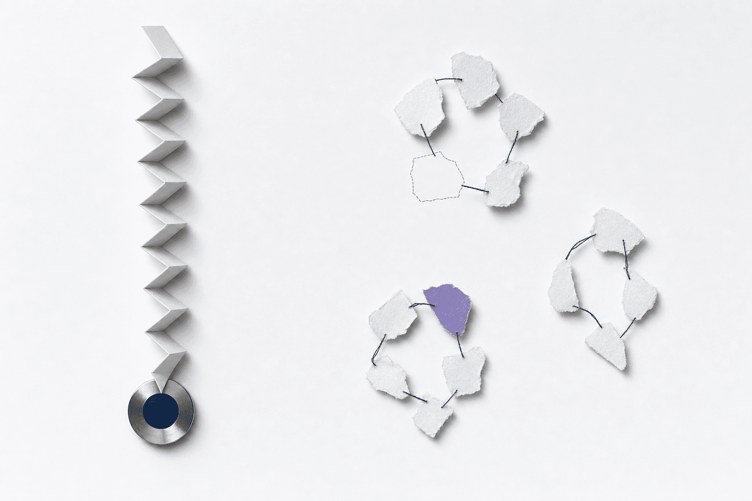 Still life: a paper strip folded into a tightening zigzag converging onto a single steel disc, beside torn paper fragments loosely grouped into three clusters linked by thread, with one fragment visibly missing.